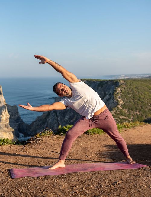 A man doing a yoga pose outdoors with a beautiful natural landscape behind him.